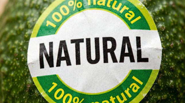 Extreme close up of a white and green circular sticker with the text natural and 100 percent natural on the bumpy green skin of a fresh avocado
