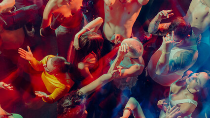Aerial view of people dancing energetically in a colorful, dimly-lit club scene. Concept of nightlife party, youth, summer, festivity, celebration