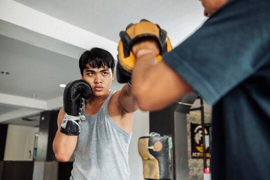 Focused young boxer throws a precise left jab to focus mitt held by coach, showing serious expression during training.