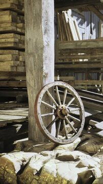 Sunlight filters through the cracks of a rustic warehouse, illuminating an old wooden wheel resting against a sturdy timber post amidst a backdrop of stacked logs and wooden beams.