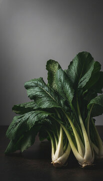 A bunch of fresh green leafy vegetables with thick white stems, presented against a muted gray background, symbolizing healthy eating and natural freshness