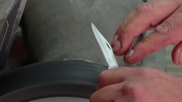 Professional Knife Sharpening in 4K Slow Motion &ndash; Close-Up of Craftsman Honing Folding Knife Blade on Rotating Sharpening Stone, Precision Blade Maintenance Workshop
