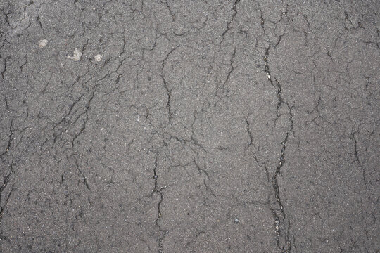 Cracked asphalt texture background with weathered grey pavement surface in city street