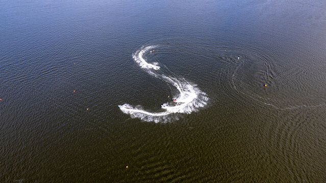 Aerial top view of jet skis forming an S-shape curve with white foam trails on water