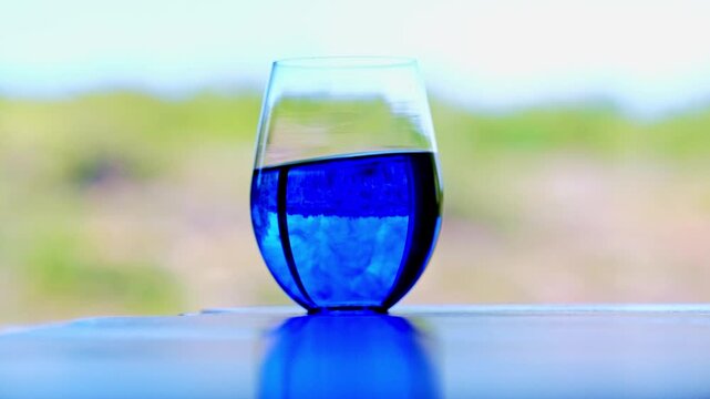 A swirling glass of Methylene Blue diluted in water on a table in front of a window