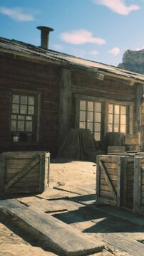 A charming wooden cabin stands in a sandy area surrounded by crates and desert terrain. The bright sky enhances the rustic scene, evoking a sense of adventure and tranquility.