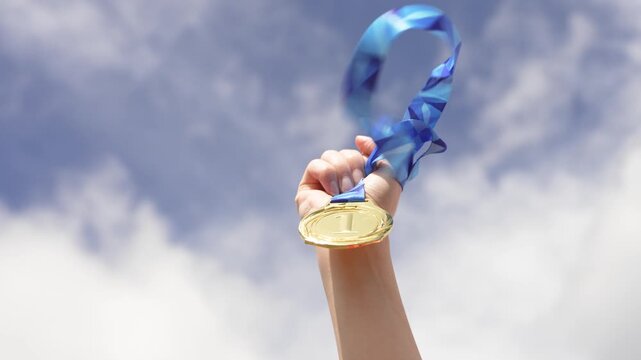 Raised hand holding a medal symbolizing success and achievement against the sky. Concept of winning, reward, recognition, and reaching goals in competition or life.
