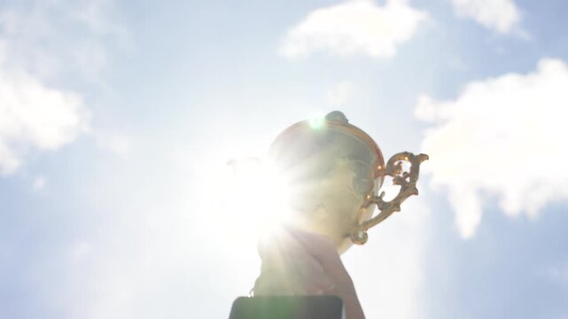 Hand holding award trophy outdoors with sky background. Concept of achievement, success, victory, recognition, and motivation. Symbol of accomplishment and celebration.