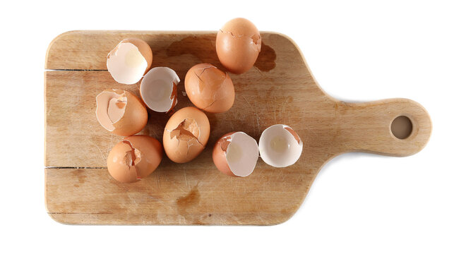 Cracked eggshell pile, crushed egg shells on chopping board isolated on white background, top view, design element