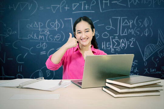 Smiling Young Asian Female Student Giving Thumbs Up with Laptop and Math Formulas Background