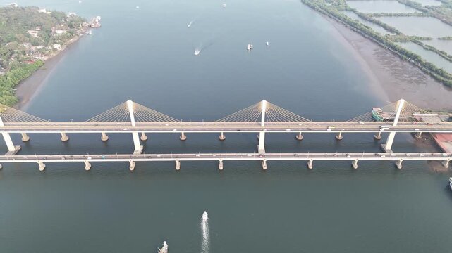 Cinematic aerial view of a modern cable-stayed bridge stretching across calm waters, with symmetrical pylons and cables forming clean geometric patterns, while boats move gently below.