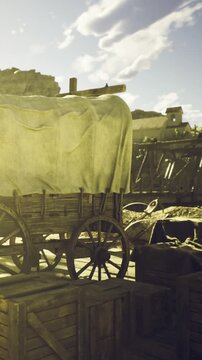 A weathered wagon sits quietly in a rustic settlement, surrounded by wooden crates. The golden light of sunset bathes the scene, creating a warm and nostalgic atmosphere.