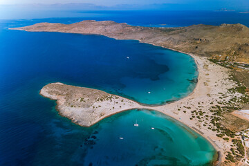 Aerial drone photograph of a the iconic rocky island peninsula of Simos beach, a Bay on the Greek island of Elafonisi (or Elafonissos) with a sandy spit, clear turquoise waters and anchored boats © Mirko