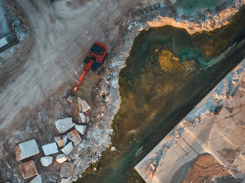 Aerial view of the Jadrankamen stone quarry featuring a red excavator, large white blocks, and a pool of water in Pucisca, Splitsko-dalmatinska, Croatia.