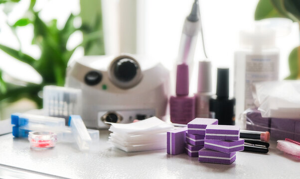 Nail drill tool, colour gel polishes, buffs and other accessories on white table