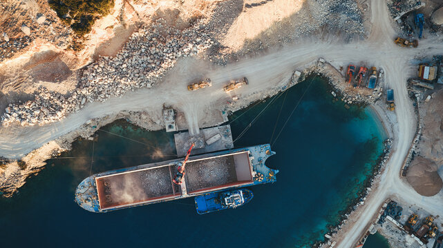 Aerial view of the Jadrankamen stone quarry with a cargo ship being loaded by heavy machinery and excavators on the coast in Pucisca, Splitsko-dalmatinska, Croatia.