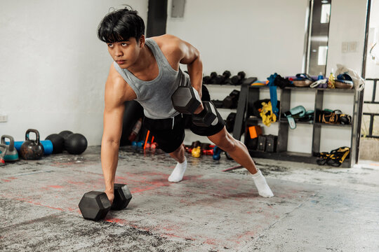 Athletic man performs alternating renegade rows with dumbbells, engaging core and back muscles while maintaining strong plank form in gym.