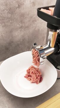 Close up of an electric meat grinder mincing fresh turkey into a white bowl. Preparation of ground meat for cooking homemade meals