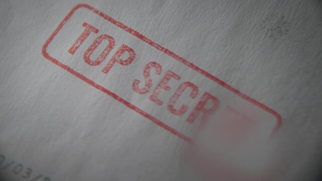 Top secret red label on classified government official sensitive document file. Close up with magnifying glass pointing at stamp of spy agency report or military intelligence confidential information