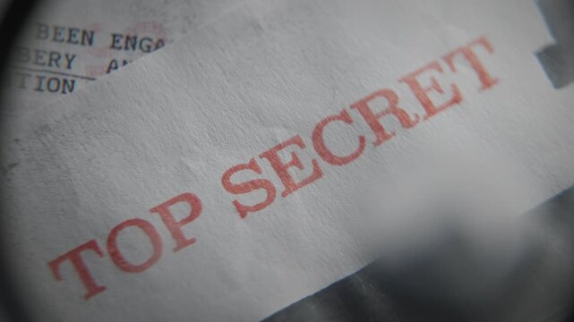 Red rubber stamp of Top Secret labeled on government confidential file document. Conspiracy or leaked information. Magnifying glass close up on old retro paper. Revealing security breach in agency