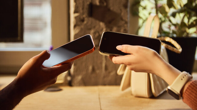 Close up of two smartphones held together for digital payment exchange. Concept of peer to peer transfer, cashless service, mobile wallet use and secure contactless transaction.