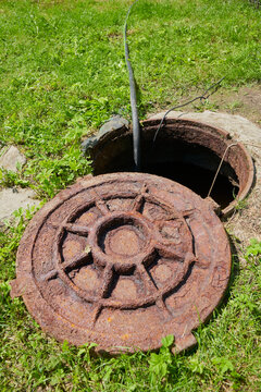 open hatch of the septic tank, rusty hatch lies on the grass near an open sewer pit on the lawn