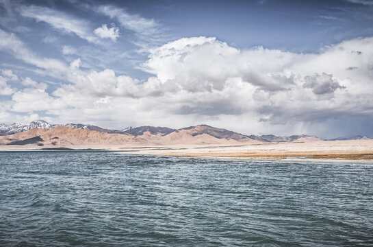 Mountain landscape, a cold high-altitude lake against the backdrop of rocky peaks and ridges with snow and glaciers, a panorama in the Tien Shan Mountains in the Pamirs, a lake with waves