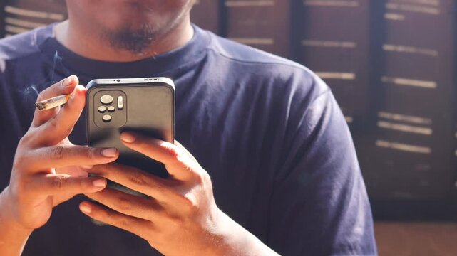 Close up of man smoking cigarette while using smartphone, typing messages or browsing social media. Bad habit, addiction and unhealthy lifestyle.