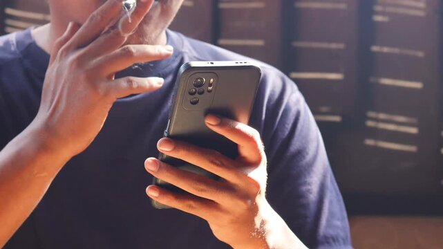 Close up of man smoking cigarette while using smartphone, typing messages or browsing social media. Bad habit, addiction and unhealthy lifestyle.