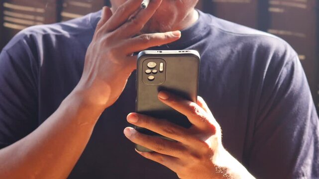 Close up of man smoking cigarette while using smartphone, typing messages or browsing social media. Bad habit, addiction and unhealthy lifestyle.