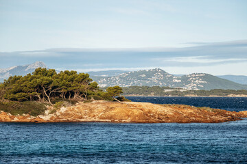 Naklejka premium Rocky islet and coastal landscape at Pointe Prime on Ile de Porquerolles with Mediterranean Sea and distant mountains under soft winter light