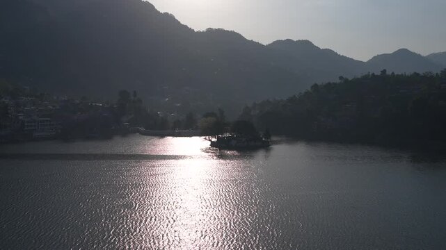 Strong sunlight creates bright reflection on still lake surrounded by dark hills