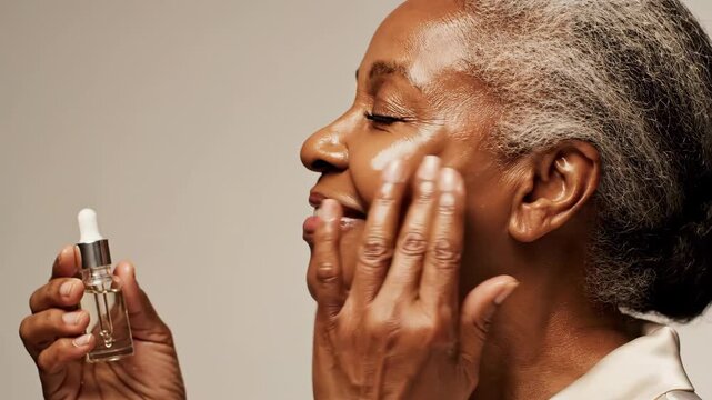mature african woman applying cosmetic serum to face from glass dropper bottle. glowing healthy skin, anti-aging beauty routine, daily self-care concept. skincare product packaging background.