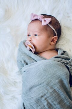 Overhead view of a newborn Baby Girl wrapped in a blanket wearing a hairband and sucking on a pacifier