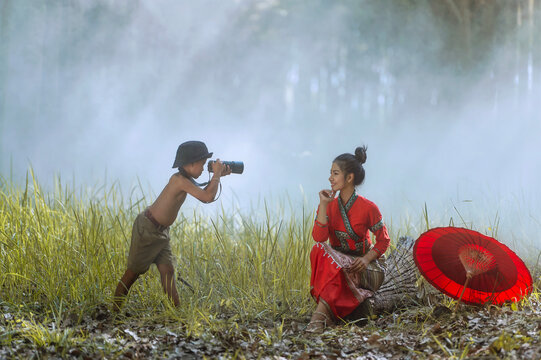 Side view of a young boy standing in a forest taking a photo of a young woman, Thailand
