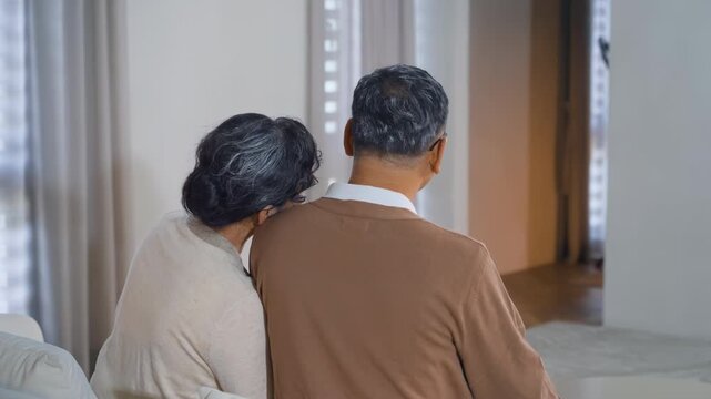 Back view of happy elderly couple wife husband sitting leaning affectionately toward each other on bed, showing the essence of love and joy shared in companionship