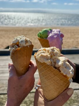 Three women standing on a promenade by a sandy beach eating traditional Danish ice cream cones on a spring day, Hjerting, Esbjerg, Jutland, Denmark