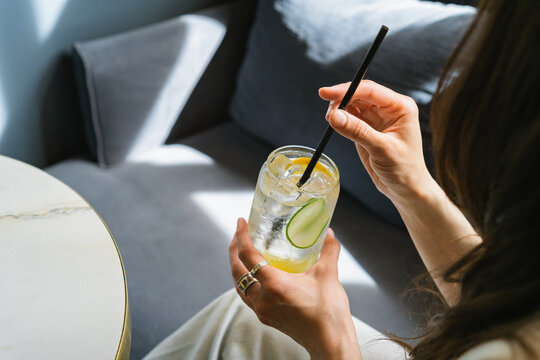Close-up of a Woman sitting at a table drinking a yuzu and melon soft drink with sliced cucumber and lemon