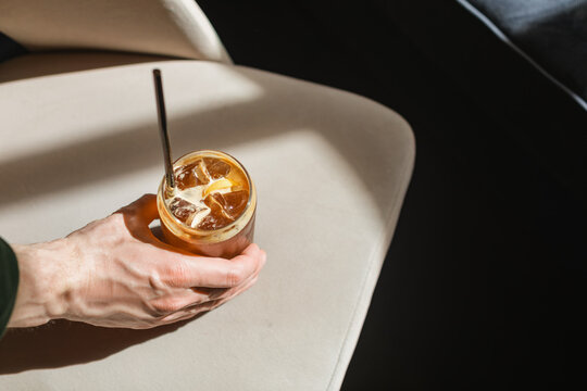Close-up overhead view of a man sitting at a table drinking an iced espresso tonic in a tall glass with a reusable metal drinking straw