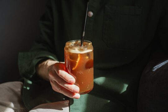 Close-up of a man holding an iced espresso tonic in a tall glass with a reusable metal drinking straw