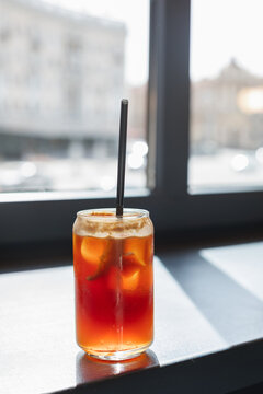 Close-up of an iced espresso tonic in a tall glass with a reusable metal drinking straw on a table in sunlight