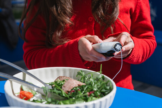 Close-up of a diabetic woman sitting at a table with a cup of black coffee and roast beef salad using an insulin pump