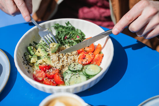 Close-up of a man sitting outdoors on a sunny day eating a healthy quinoa salad with fresh avocado, cucumber, tomato, red pepper and rocket