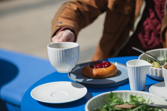 Close-up of a man sitting at a table drinking a cup of coffee and eating a roast beef salad and cherry brioche bun