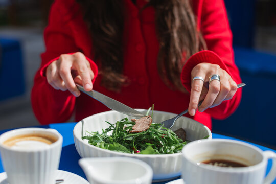 Close-up of a woman sitting at an outdoor cafe enjoying a roast beef salad and coffee