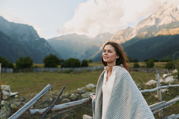 Naklejka premium A woman in a light poncho stands in a mountain meadow, enjoying open sky and fresh air. A tranquil, nature inspired lifestyle moment.