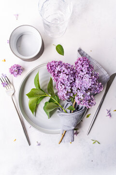 Close-up overhead view of a rustic spring place setting on a table with fresh lilac flowers