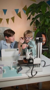 Kids examine and test a 3D printed part in their hands, near working 3D printer