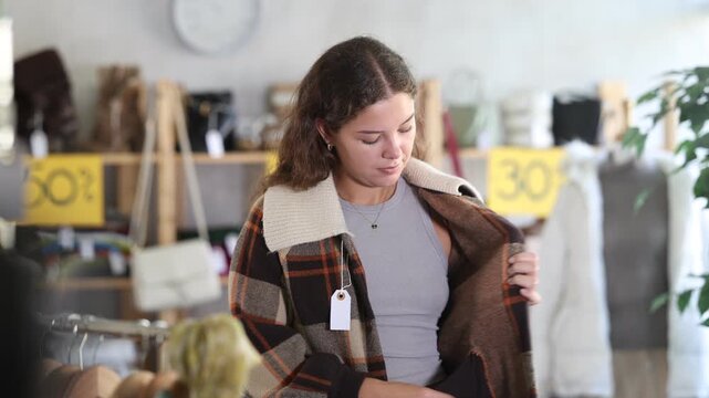 Smiling young woman posing in short checkered coat while shopping in retail outlet
