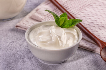 Creamy plain yogurt in white bowl with fresh mint garnish on stone table © Andrei Starostin